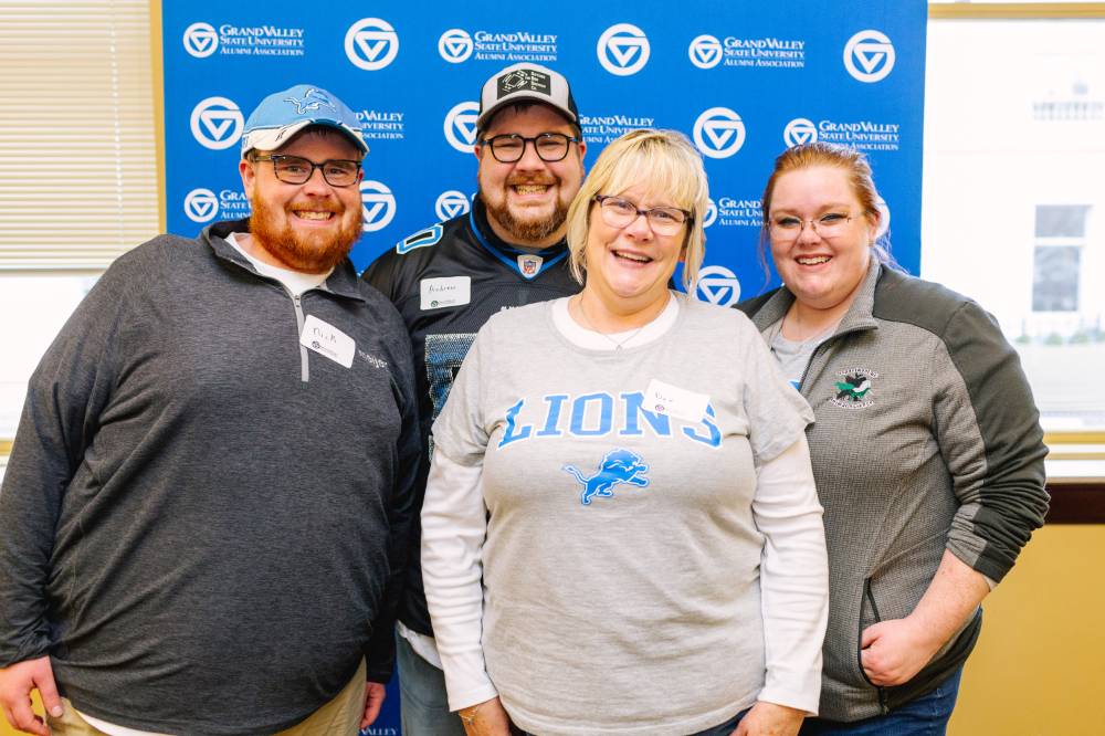 A family smiles for a photo in front of the GVSU backdrop